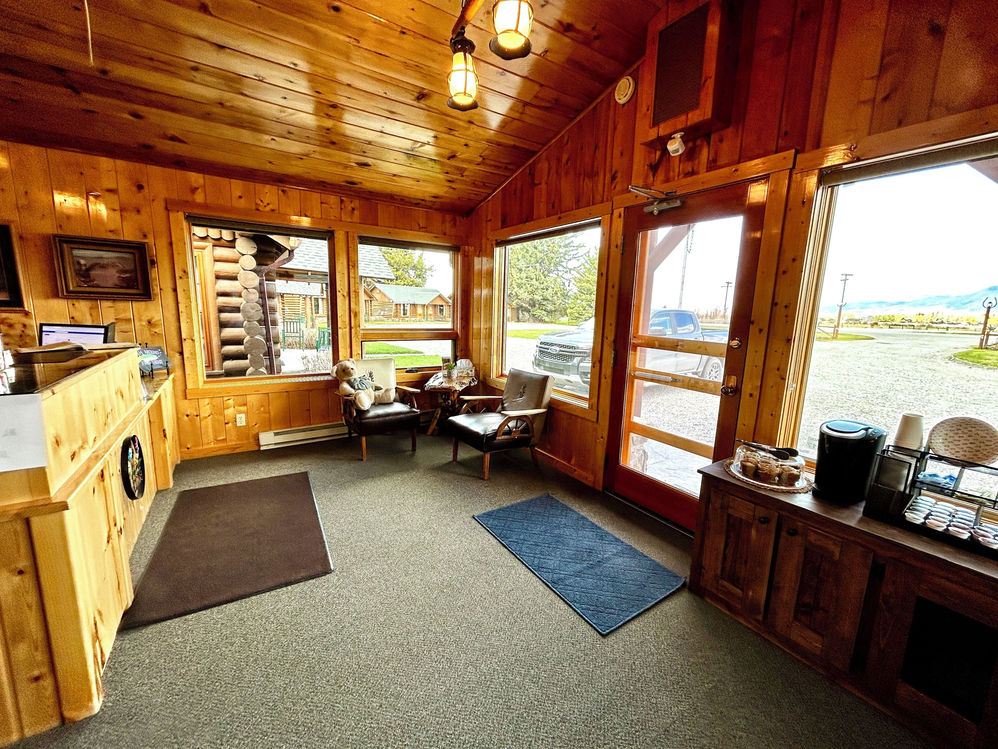 L’intérieur d’un chalet accueillant, avec des murs en bois, un comptoir d’accueil, un coin salon avec des fauteuils, une machine à café et une vue sur l’extérieur.