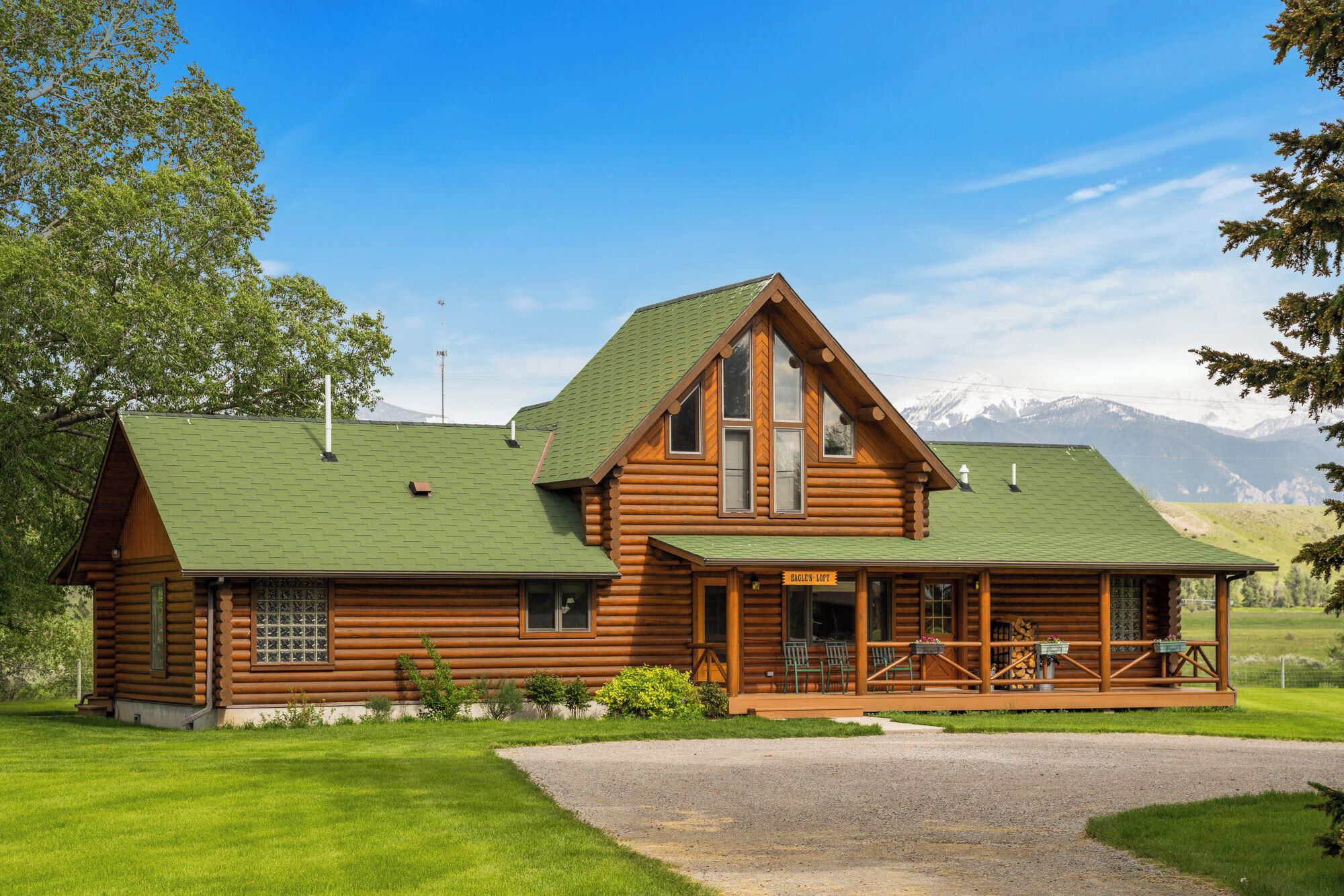 A log cabin with a green roof, a porch with outdoor seating, and a sign reading "Eagle's Lodge".