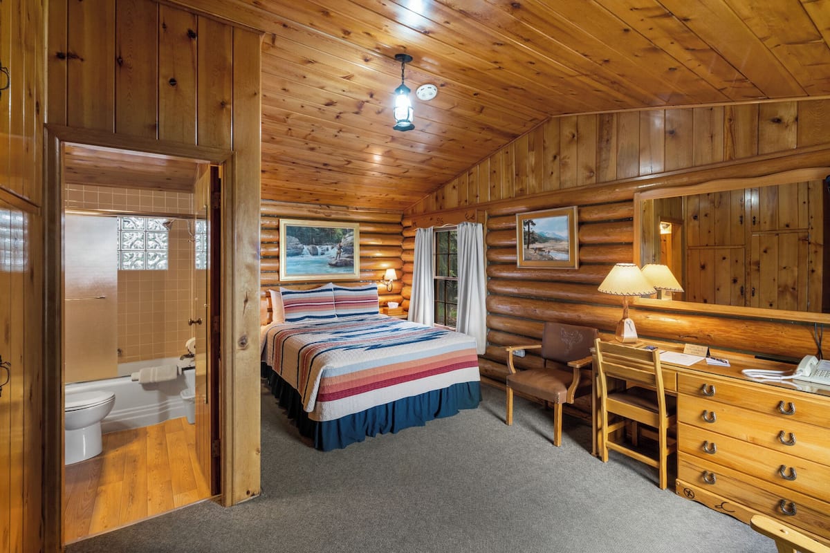 Ein Schlafzimmer in einer Blockhütte mit Bett, Schreibtisch, Stuhl und Spiegel.