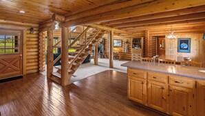 L’intérieur d’une cabane en rondins présente un escalier central, des planchers en bois, un coin cuisine avec des meubles en bois et un coin repas.