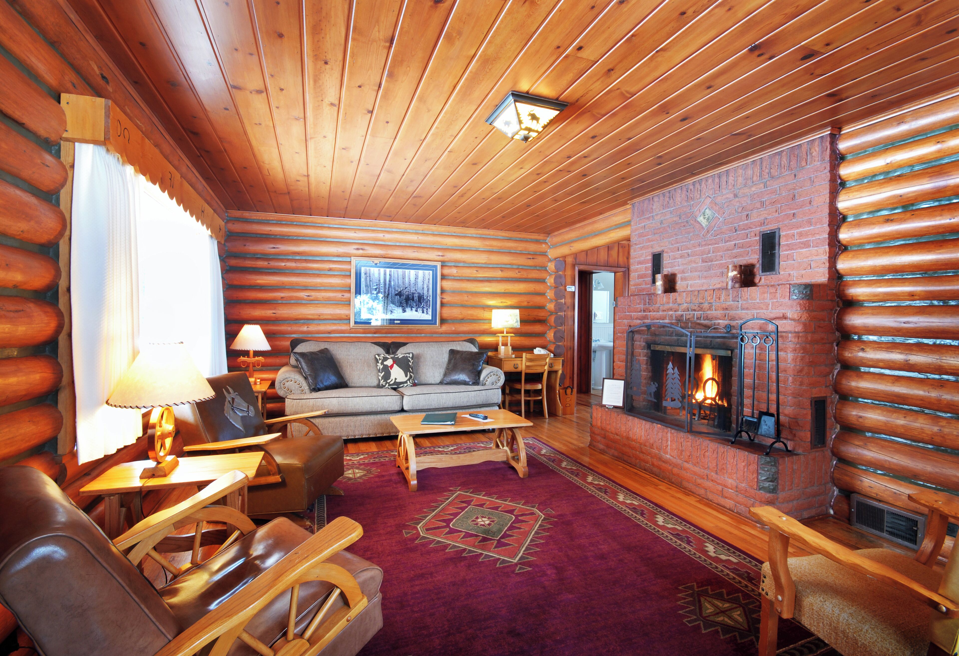 Interior de una cabaña de troncos con chimenea, muebles de madera y una zona de estar acogedora.