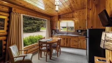 Una cocina acogedora estilo cabaña, con armarios de madera, un comedor con mesa y sillas, un refrigerador y una ventana con vistas a la vegetación.