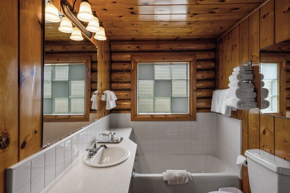 A wooden cabin bathroom with a sink, mirror, and bathtub. - El Western Cabins & Lodges (Ennis)