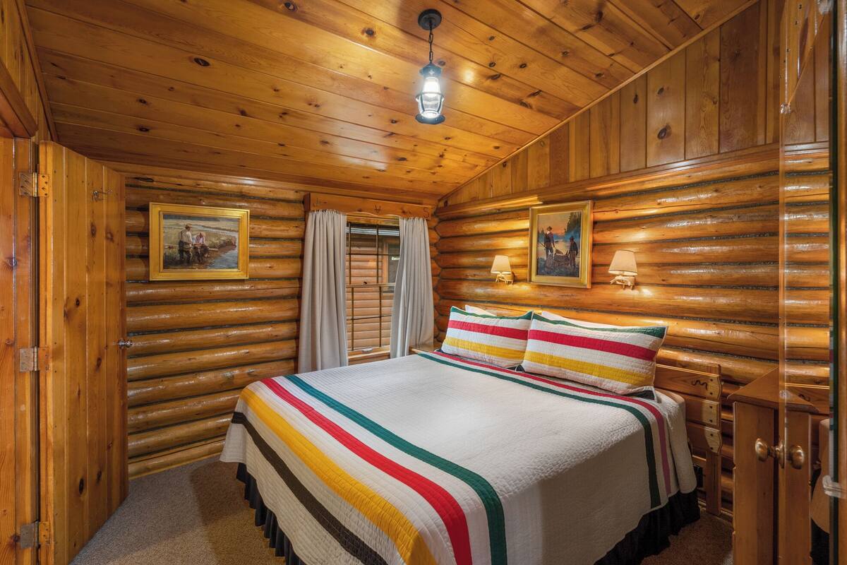 Ein Schlafzimmer in einer Blockhütte mit einem Bett, zwei Wandlampen und zwei gerahmten Bildern.