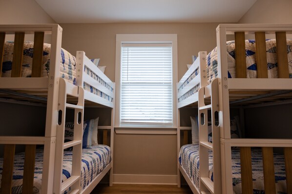 A room with bunk beds, a window with blinds, and a wooden floor. - Magnolia By The Bay – A charming 3-bedroom, 2-bath cottage in Perdido Beach, AL (Elberta)
