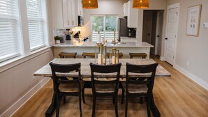 Een moderne keuken met witte kasten, een groot eiland en hangende lampen.