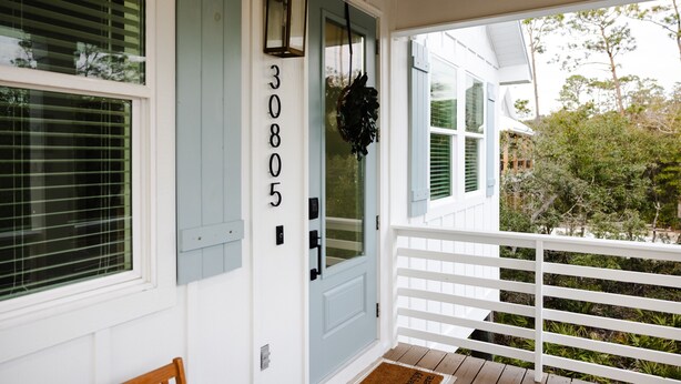Een huis met nummer 30805 op de deur, een veranda met witte railing en een houten terras.