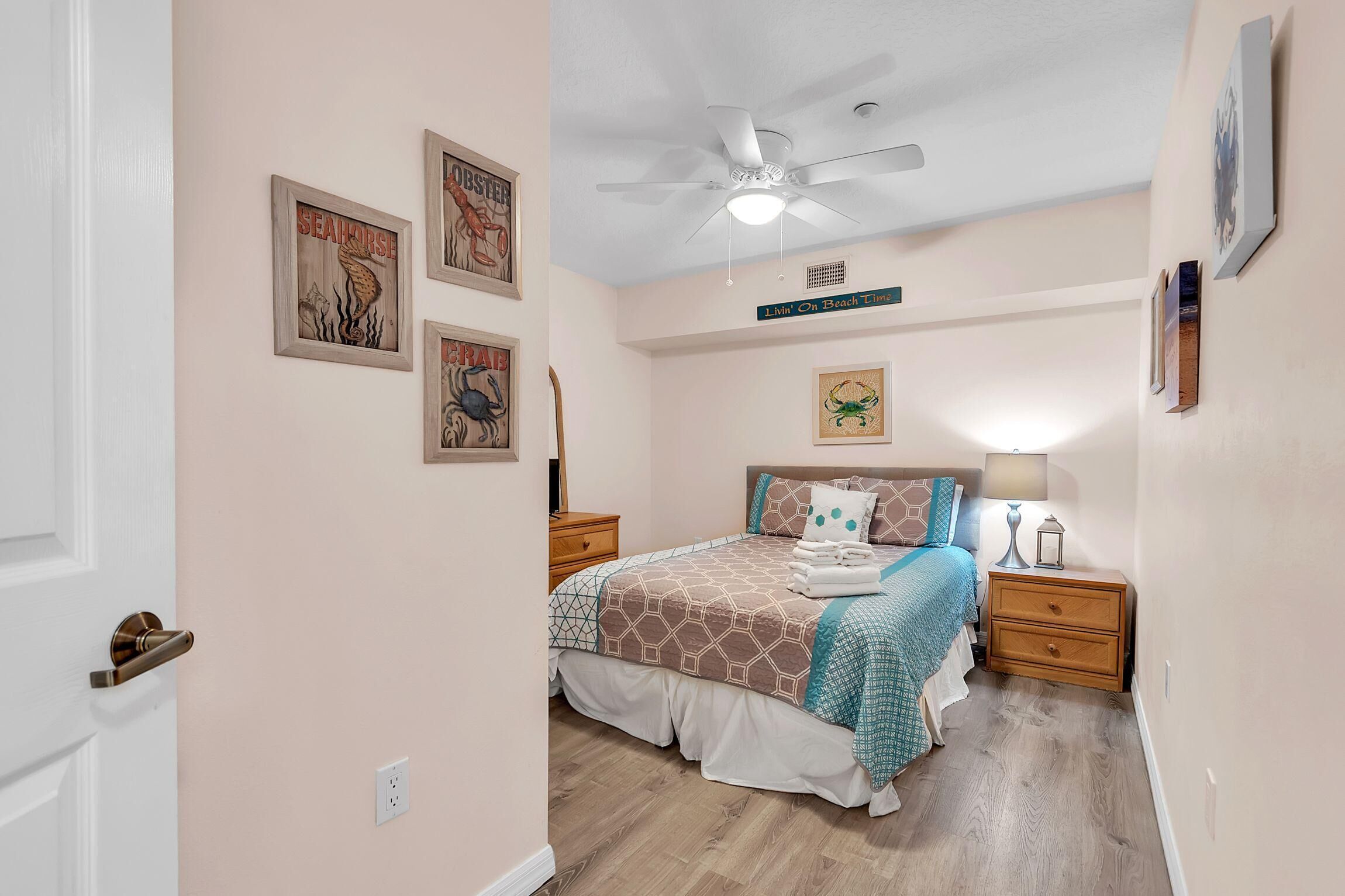 A bedroom with a bed, nightstands, a ceiling fan, and wall art.