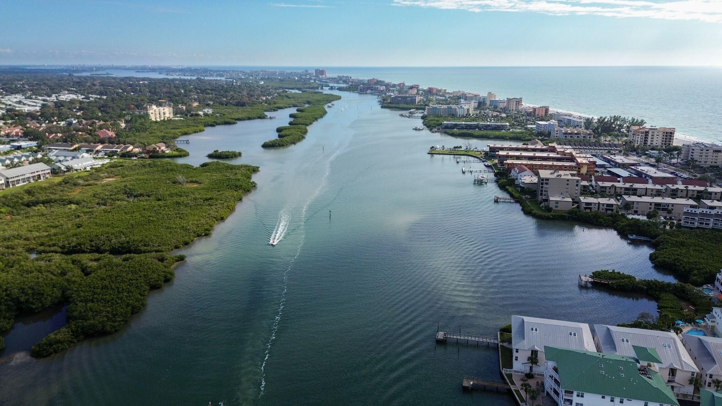 An aerial view of a coastal city with a river running through it, surrounded by dense greenery and urban development.