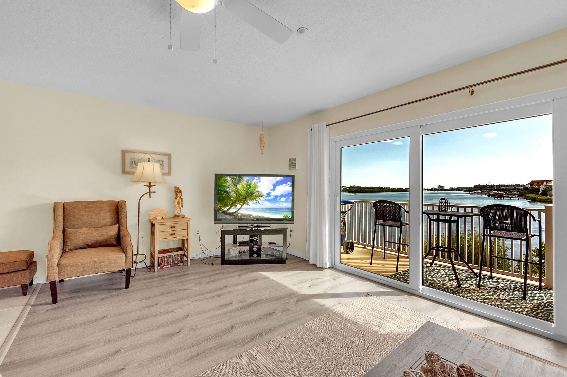 A living room with a TV, a sofa, a lamp, and a view of a balcony with outdoor furniture.