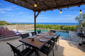 Ein Essbereich im Freien mit Blick auf das Meer, ein Pool und ein Grill.