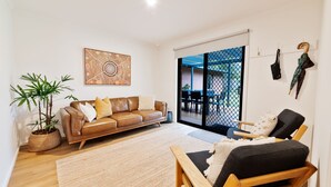 Un salon avec un canapé en cuir marron, un fauteuil noir, une grande peinture abstraite, une plante en pot et une porte-fenêtre coulissante donnant sur un espace extérieur.
