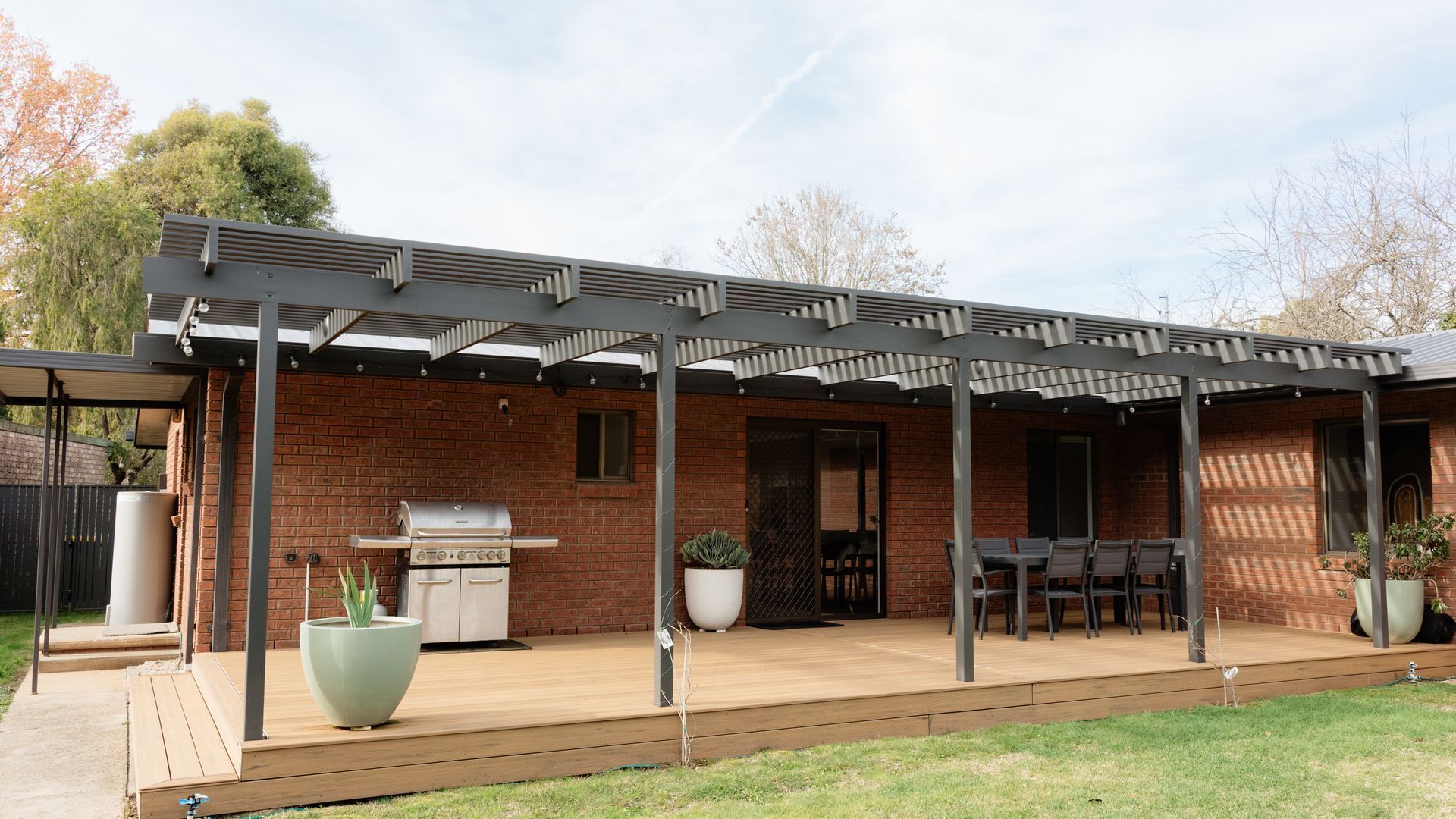 Un patio couvert comprenant un barbecue, des sièges d’extérieur et des plantes en pot.