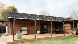 Un patio couvert comprenant un barbecue, des sièges d’extérieur et des plantes en pot.