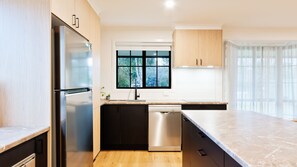 A modern kitchen with a stainless steel refrigerator, dishwasher, and a window with a view of trees. - Halinka Haven - Family Friendly, Close to Town (Bright)