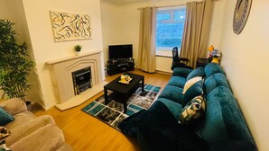 A living room with a fireplace, a sofa, a television, and a window with curtains. - Comfortable 2-Bed Flat in Heart of Tyne & Wear - Pass the Keys (North Shields)