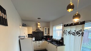 A compact kitchen with black and white cabinetry, a dining table with a vase of flowers, and pendant lights. - Comfortable 2-Bed Flat in Heart of Tyne & Wear - Pass the Keys (North Shields)