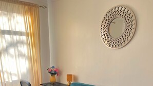 A teal sofa with patterned cushions, a small table with a vase of flowers, and a decorative mirror on the wall. - Comfortable 2-Bed Flat in Heart of Tyne & Wear - Pass the Keys (North Shields)