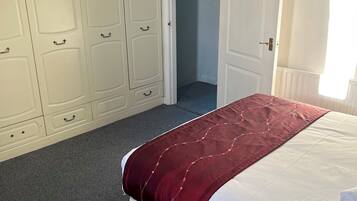 A bedroom with a large white wardrobe, a bed with a red blanket, and a view of a hallway.