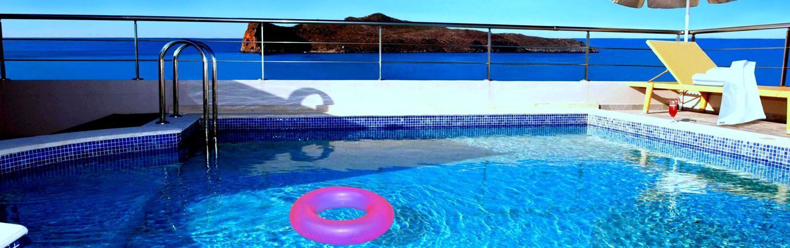 A swimming pool with a pink float ring, a metal ladder, and a view of the sea.