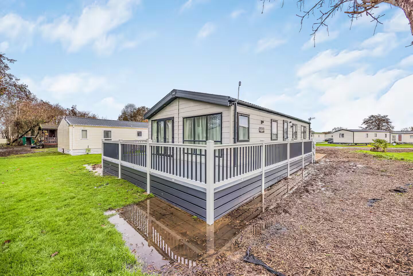 A mobile home with a fenced deck, a grassy yard, and a clear sky.
