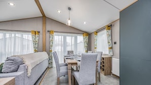 Una habitación moderna con sofá, mesa de comedor, sillas y ventanas amplias con cortinas.