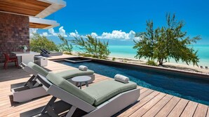 A modern poolside area with lounge chairs, a small table, and a view of the ocean. - Beachfront Villa w/ Pool & Ocean Views (Long Bay)