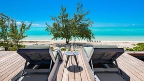 A wooden deck with lounge chairs facing a beach and ocean view. - Beachfront Villa w/ Pool & Ocean Views (Long Bay)