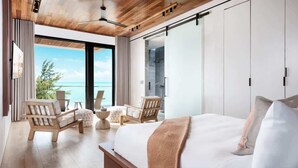 A modern bedroom with a large bed, wooden furniture, and a view of the ocean. - Beachfront Villa w/ Pool & Ocean Views (Long Bay)