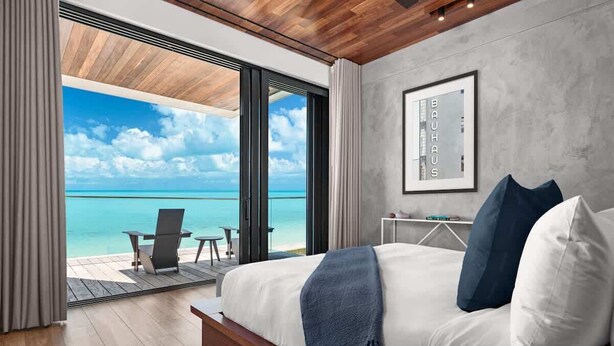 A modern bedroom with a large bed, a view of the ocean, and a framed picture on the wall. - Beachfront Villa w/ Pool & Ocean Views (Long Bay)