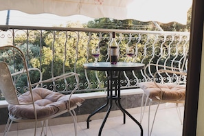 Een balkon met een ronde tafel en twee stoelen, een fles wijn en twee glazen op de tafel.