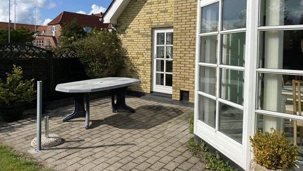 A courtyard with a table and chairs, a brick building with large windows, and a clear sky. - 4 Star Holiday Home in Hals (Hals)