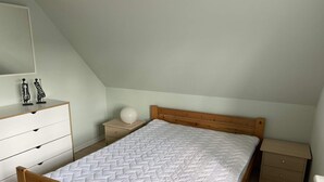A bedroom with a wooden bed, a white dresser, a bedside table with a lamp, and a small nightstand. - 4 Star Holiday Home in Hals (Hals)