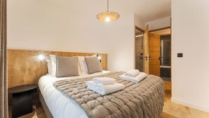 Een moderne slaapkamer met een houten hoofdbord, een groot bed met een gewatteerde hoes, twee kussens, een nachtkastje en een hangende lamp.