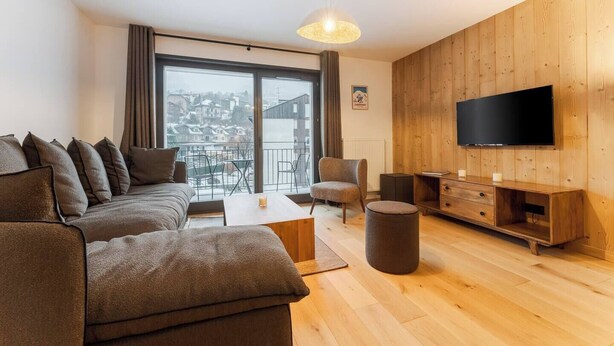 Een moderne woonkamer met een bank, fauteuil, salontafel en televisie.
