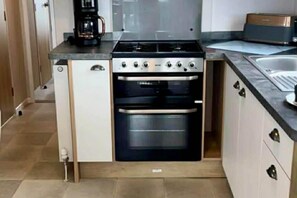 Eine kleine Küche mit Herd, Backofen und einer Kaffeemaschine auf der Arbeitsplatte.