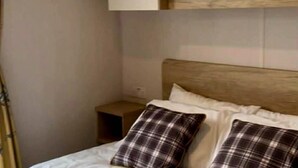 Un dormitorio con cabecera de madera, dos almohadas a cuadros, una colcha blanca y una mesita de noche pequeña.