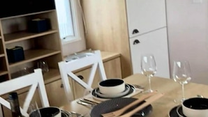 Un comedor con una mesa dispuesta para dos, un televisor al fondo y un armario blanco a la derecha.