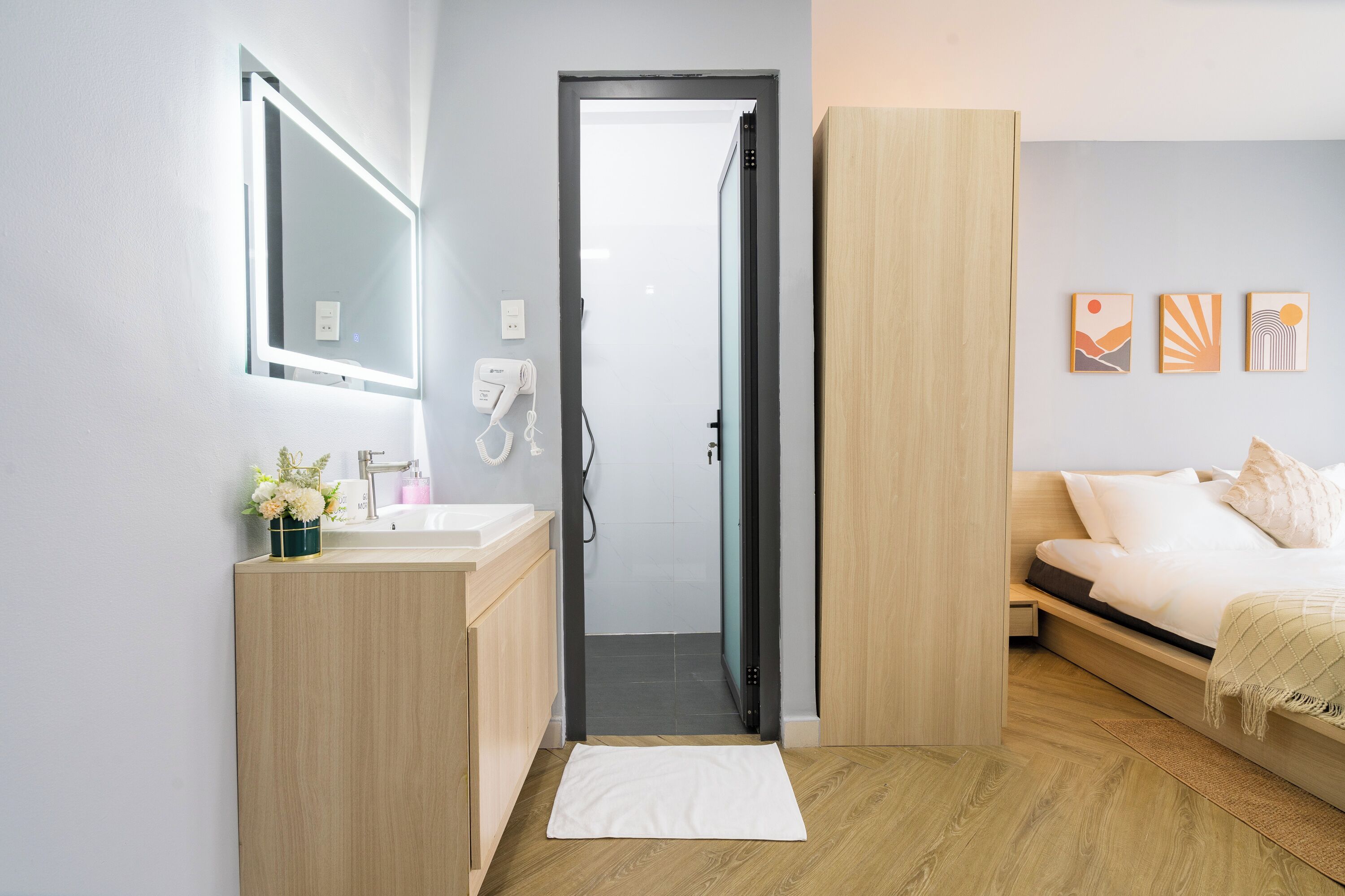 Una habitación de hotel moderna con un tocador de madera, un espejo, una cama con edredón blanco y una mesita de noche pequeña.