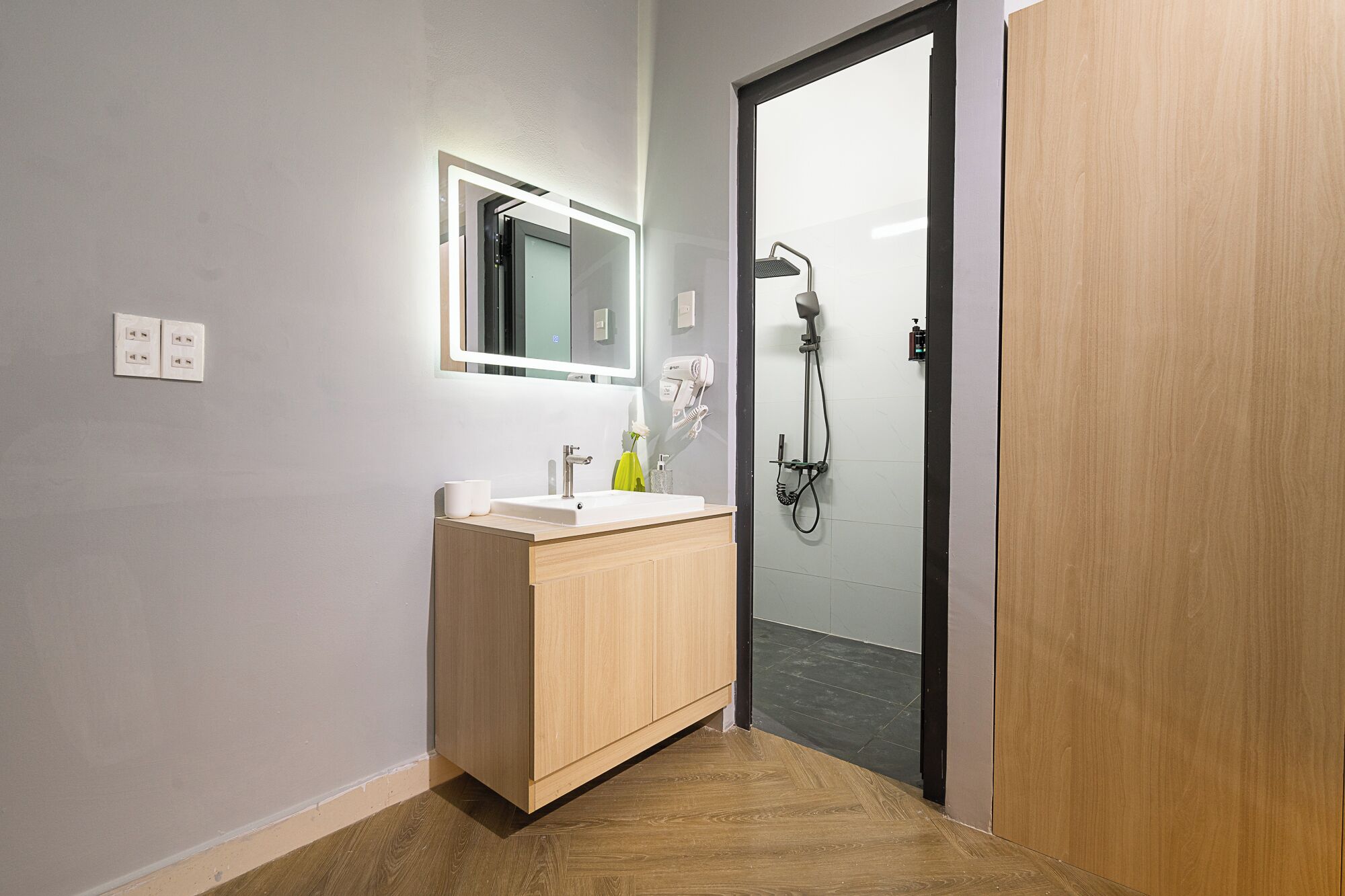 A modern bathroom with a wooden vanity, a mirror, a shower, and a door.