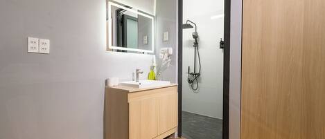 A modern bathroom with a wooden vanity, a mirror, a shower, and a door.