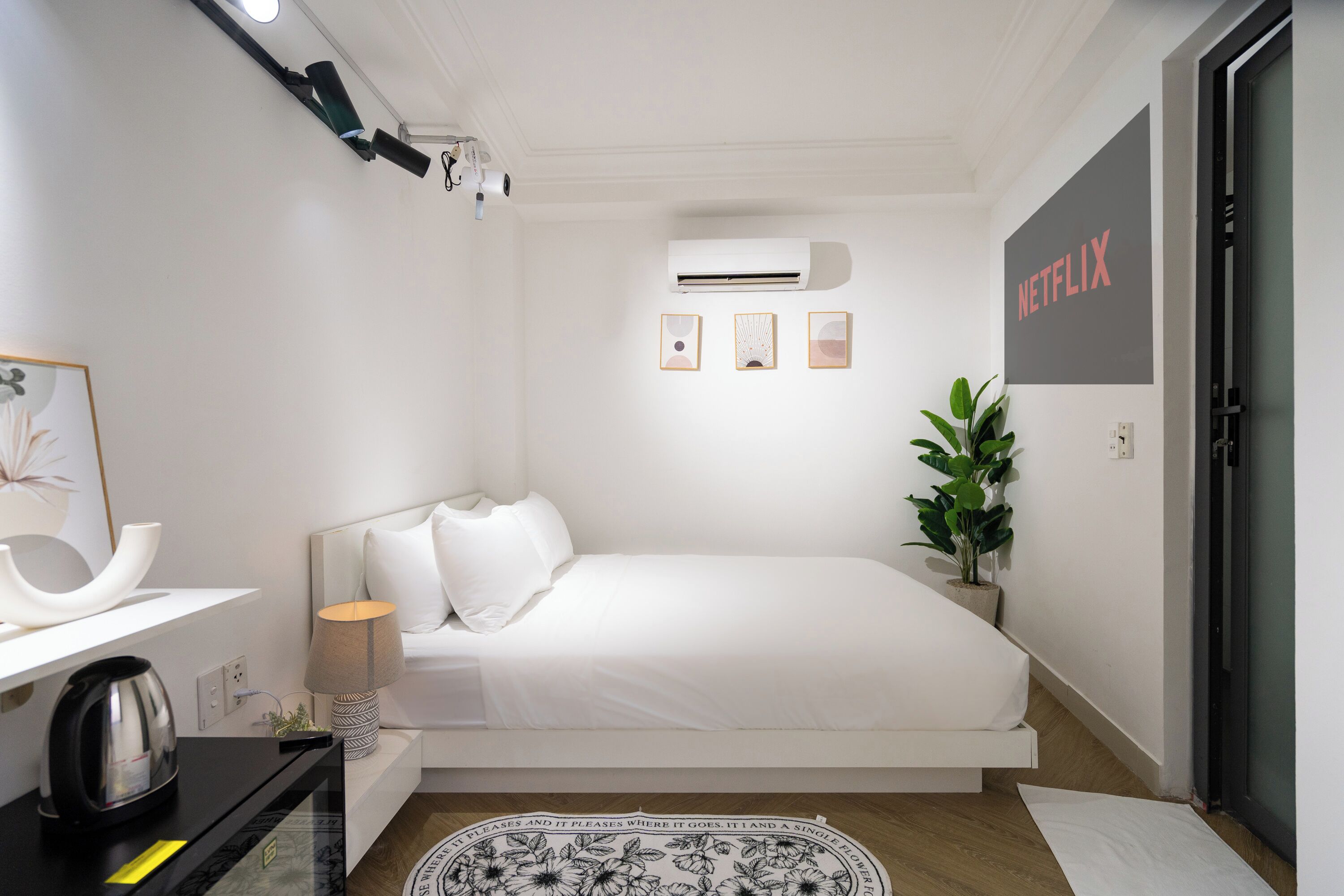 Un dormitorio moderno con cama, lámpara de noche, equipo de aire acondicionado y un letrero de Netflix en la pared.