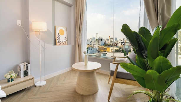 A modern room with a large window, a round wooden table, a floor lamp, and a potted plant. - Chill Hill Hotel & Home (Ho Chi Minh City)