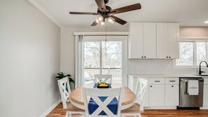 A modern kitchen with white cabinets, a wooden dining table, and a ceiling fan. - Family friendly, Youth Sports tournaments, World Cup-Ready, Lenexa, 3BR Near KC (Lenexa)