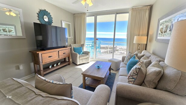 A living room with a TV, wooden furniture, a sofa, and a view of the beach. - Beach Club B502 -Direct Gulf View-Right On The Beach-Pool/Hot Tub-WiFi! Sleeps 5 (Gulf Shores)