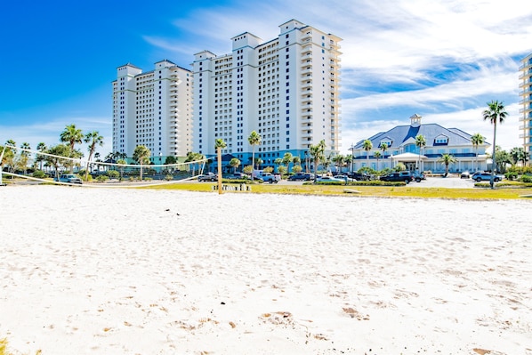 A beachfront hotel with multiple high-rise buildings, a sandy beach, and a parking area with cars.