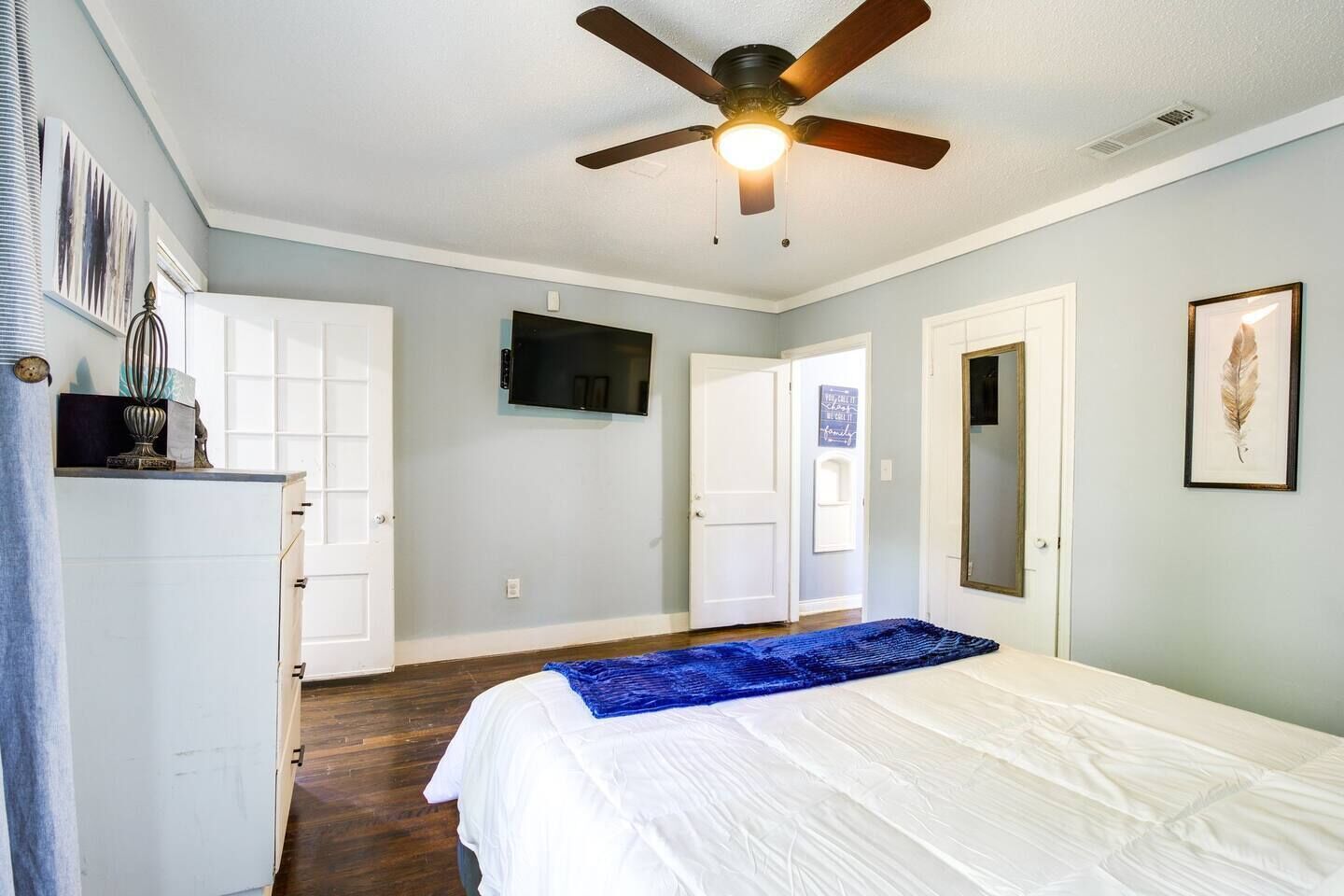Un dormitorio con cama, ventilador de techo, televisor y una puerta.