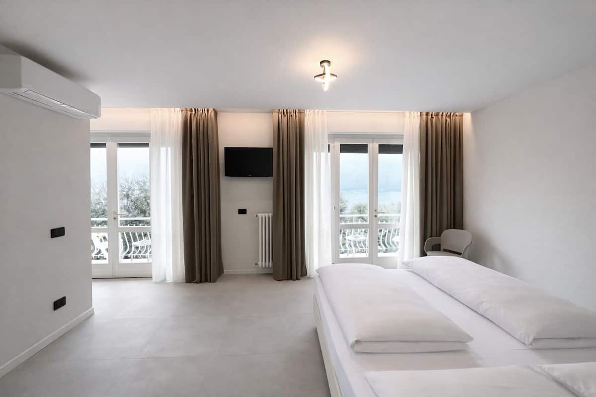 Una habitación de hotel moderna con cama, televisor y balcón con cortinas.
