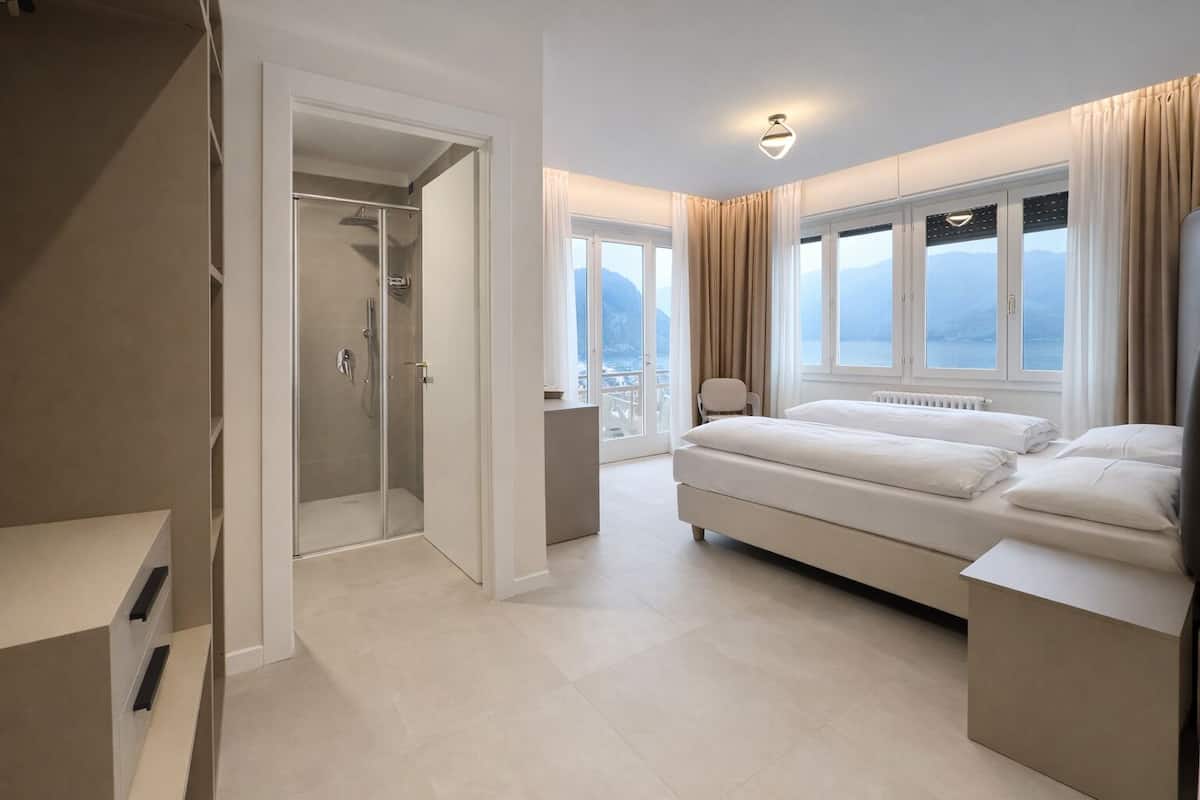 Una habitación de hotel moderna con una cama grande, un vestidor, zona de ducha y un balcón con vistas.