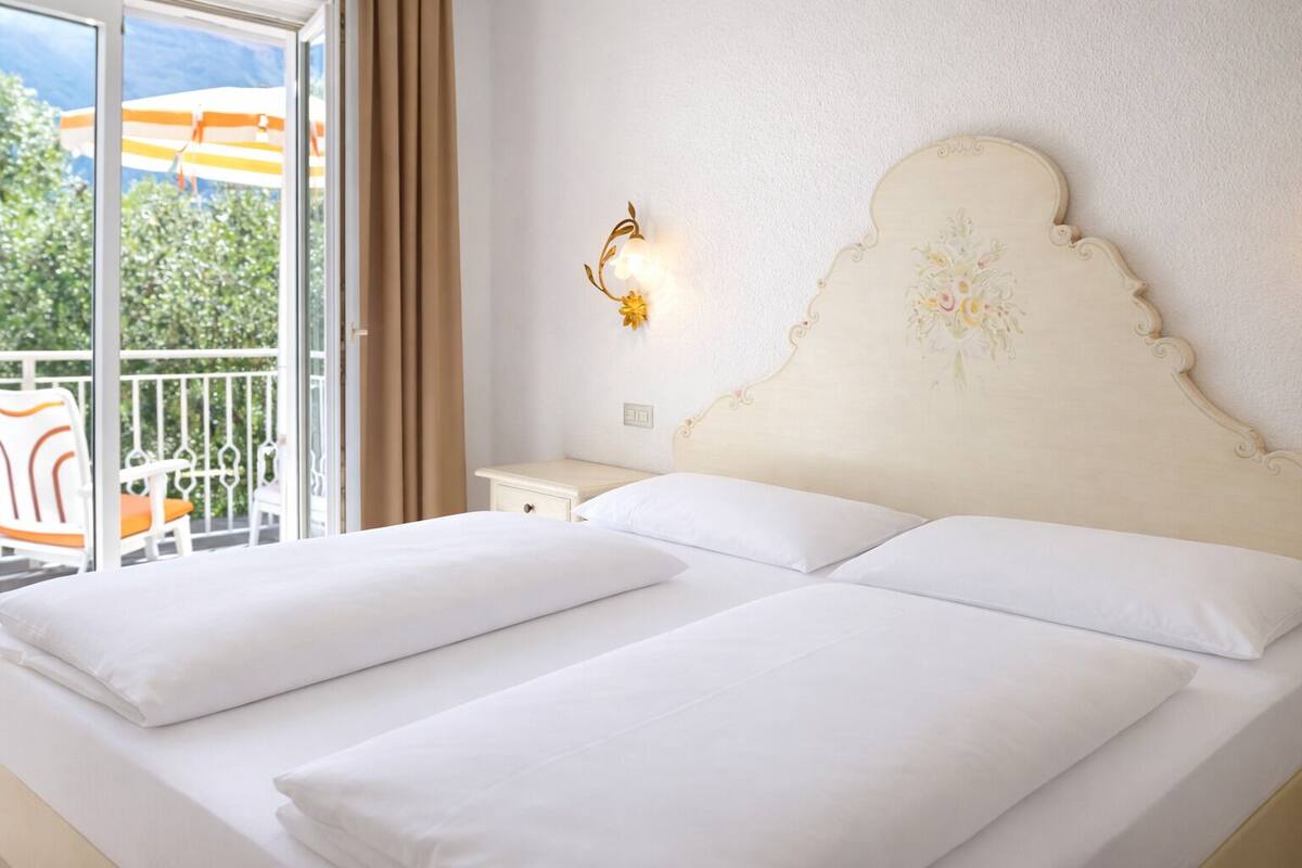 Una cama doble con sábanas blancas en una habitación de hotel con balcón.